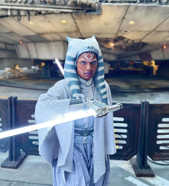 Ahsoka Tano cosplayer in a custom live-action headpiece, holding a lit lightsaber