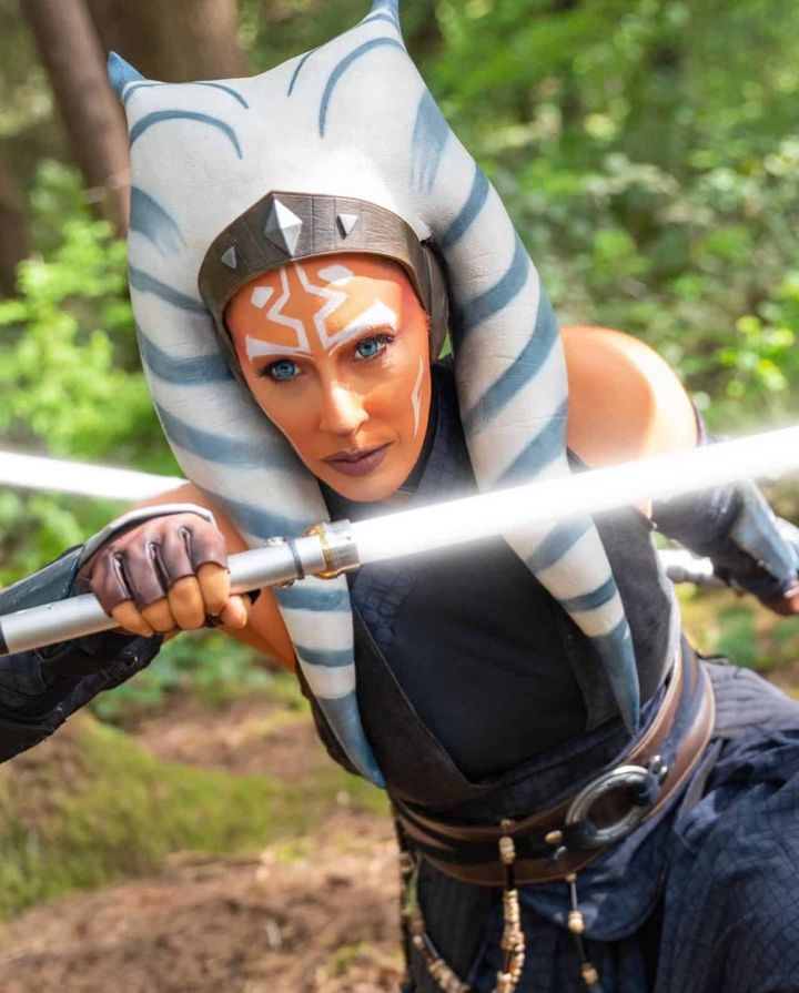 Ahsoka Tano cosplayer kneeling with a lightsaber in a forest
