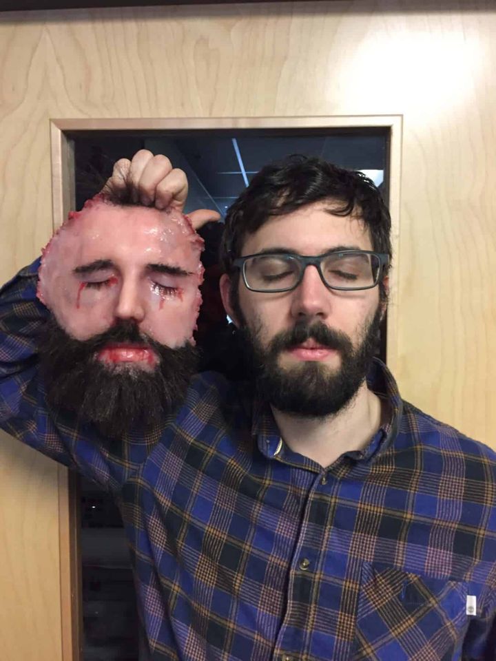 Man holding up a silicone replica of his own face beside him